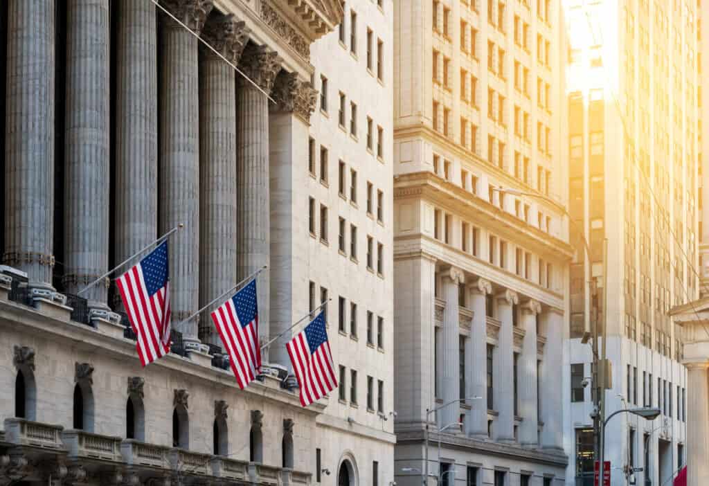 American flags flying in front of the historic buildings of Wall Street